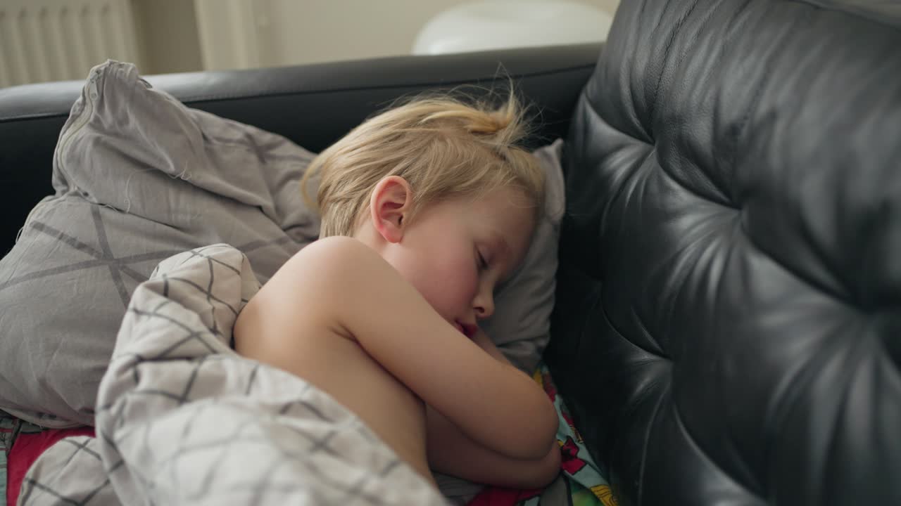 7살의 백인 소년이 검은색 소파에 누워서 메스꺼움 속에 잠을 자려고 하는 순간