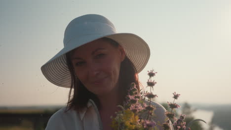 woman wearing white hat gently scent wildflowers in her hand under soft morning sun, backlit by glowing light with peaceful expression, capturing serene outdoor moment filled with nature and calm
