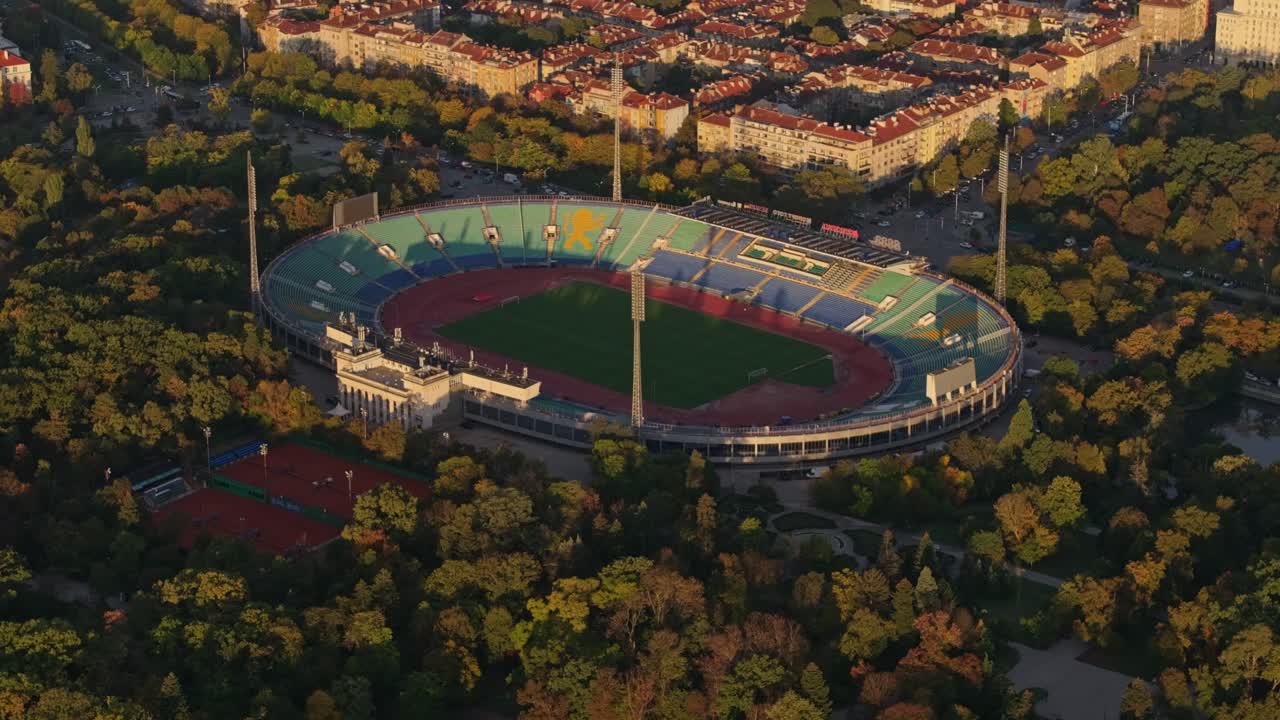 Ujęcie z lotu ptaka stadionu oświetlonego świtem, z drogą i dachami, Bułgaria