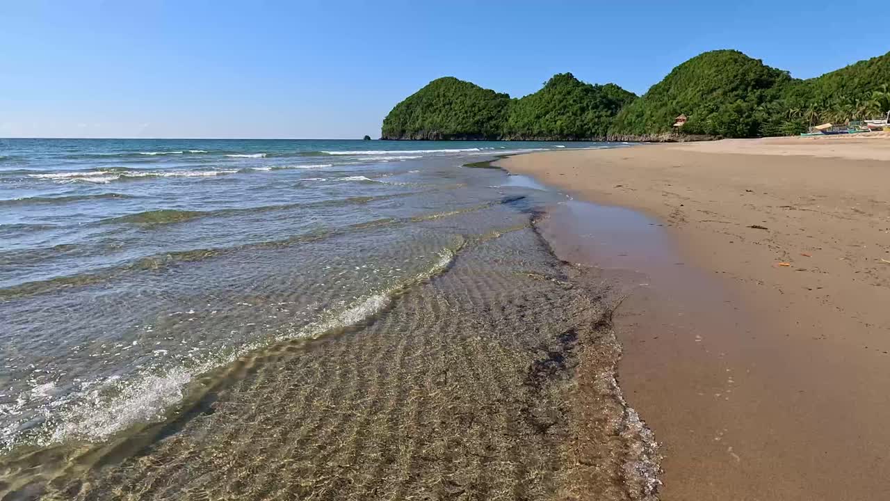 Spiaggia tranquilla e da sogno con onde morbide e scintillanti e isole verdi distanti sotto un cielo limpido e soleggiato a Sugar Beach Sipalay, Negros Occidental, Filippine.