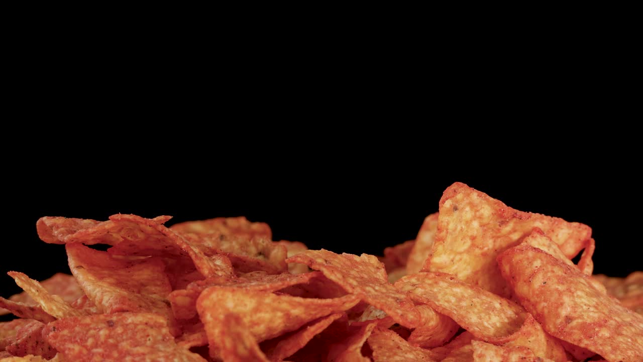 Tortilla chips che cadono a rallentatore su una pila, la cui consistenza croccante è messa in risalto da un'illuminazione intensa