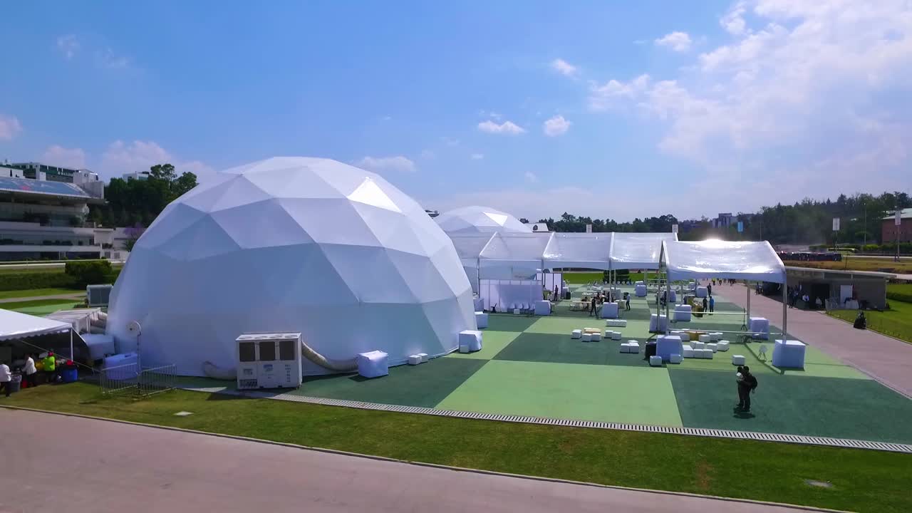 A drone flying over a stadium with spherical tents.