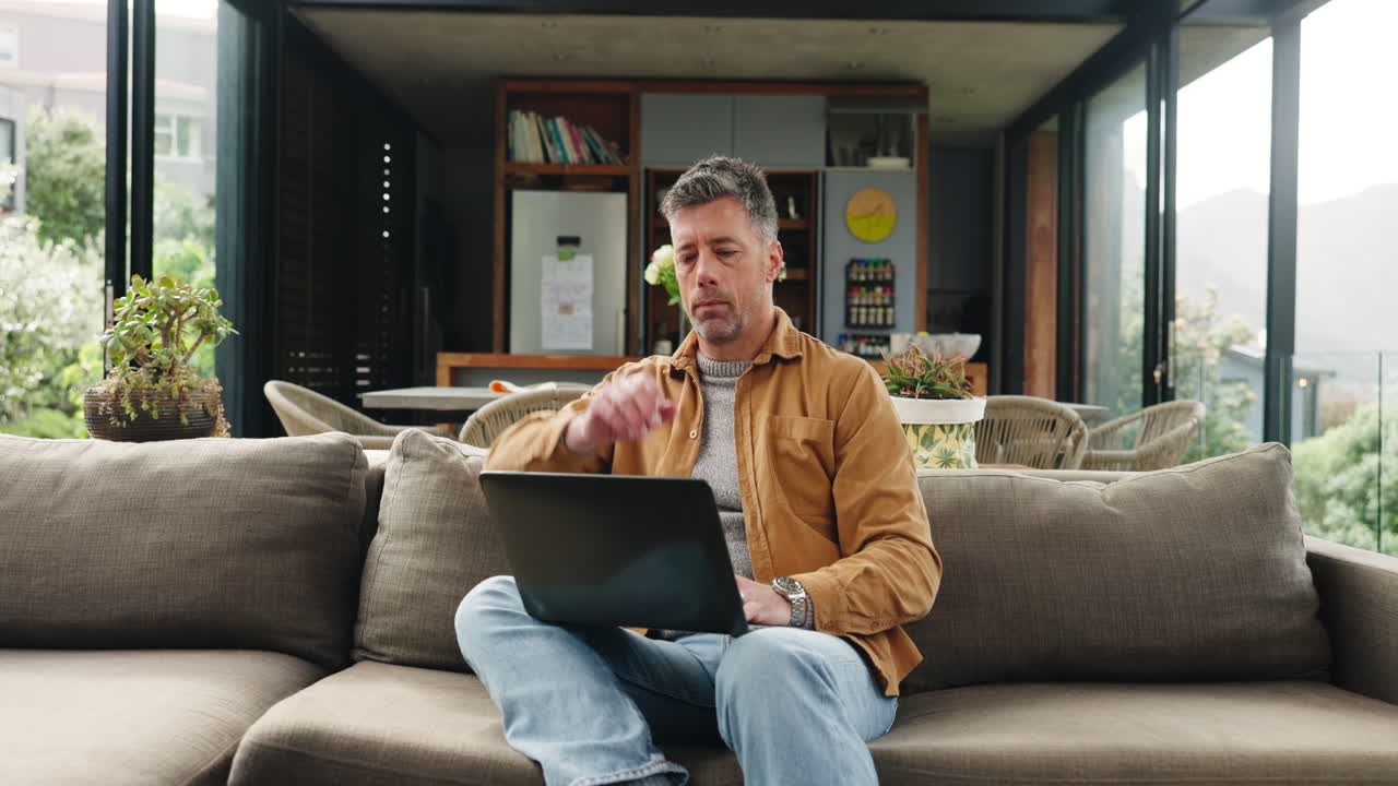 Focused Man Working on Laptop While Sitting on Couch at Home