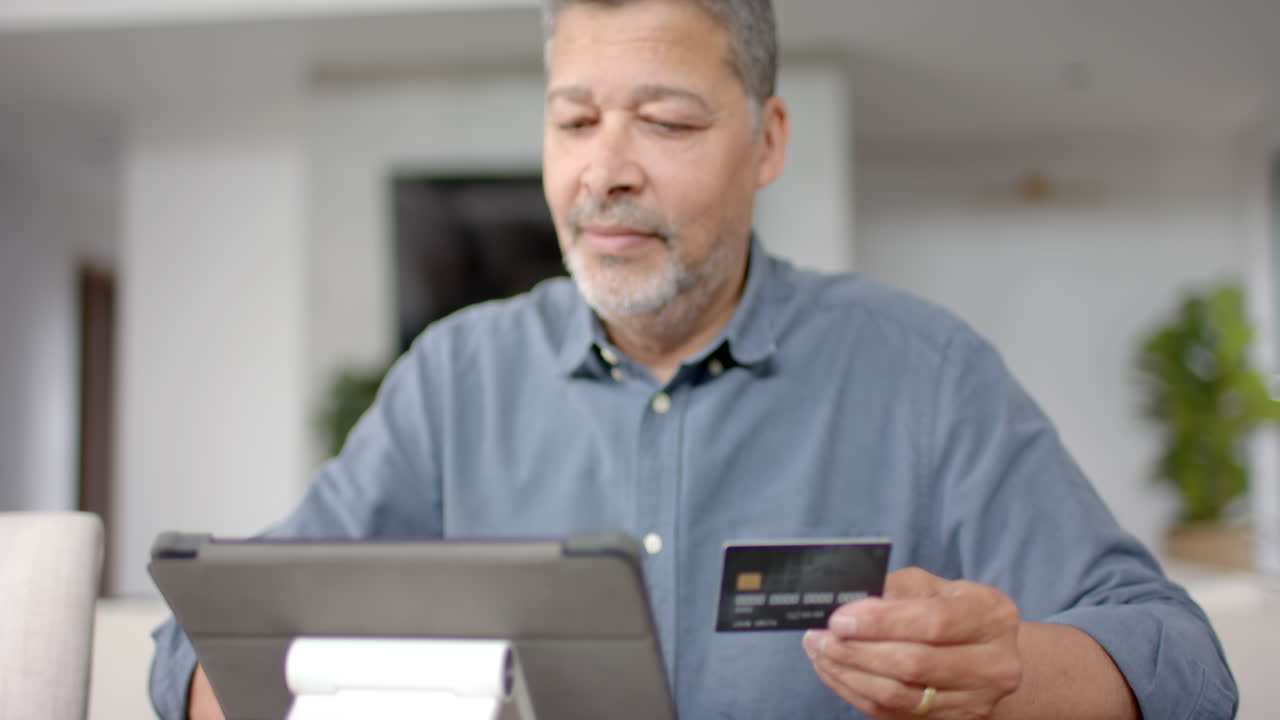Uomo anziano birazziale felice che usa carta di credito e tablet per pagamenti online, in slow motion