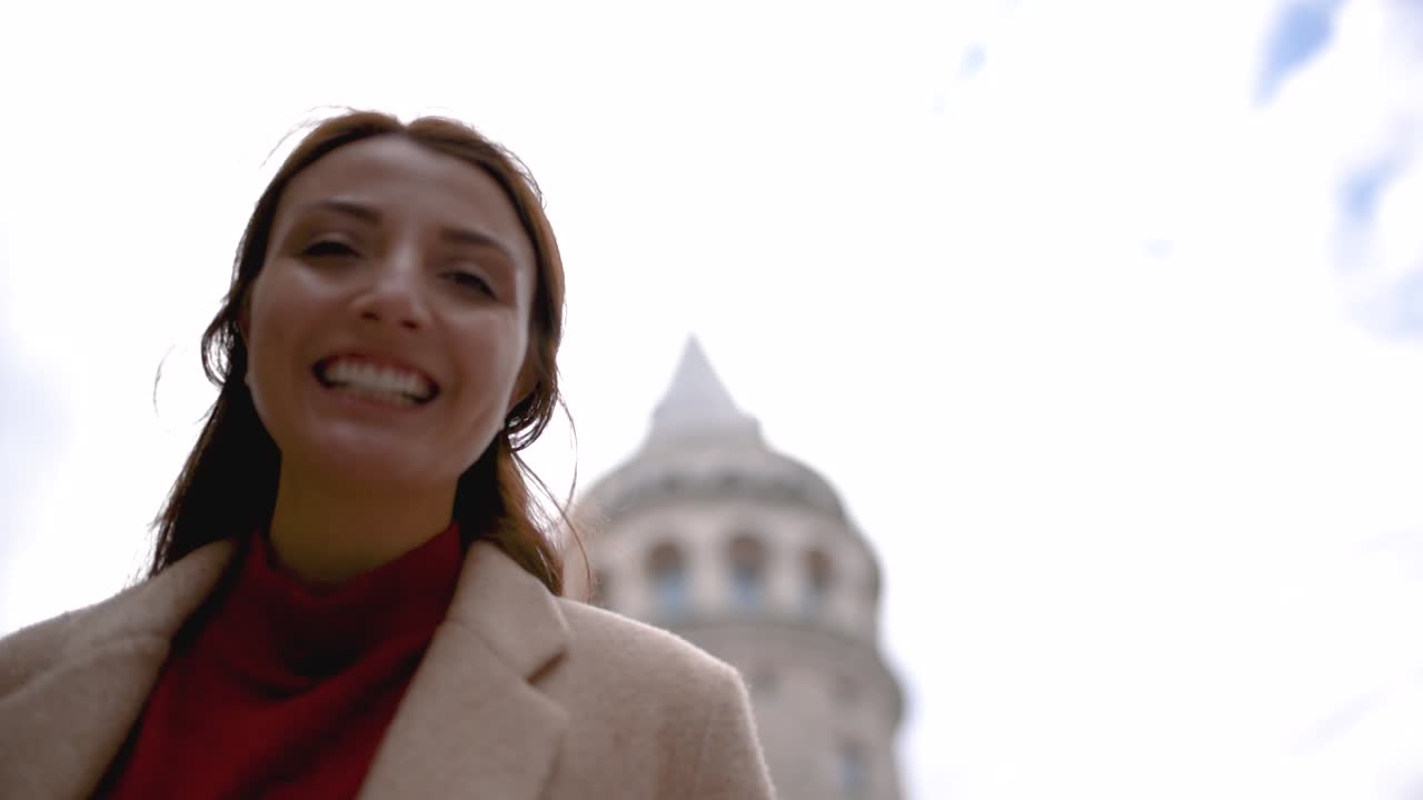 Jovem bonita com roupas elegantes segura e usa uma máscara descartável, com vista para a Torre Galata ao fundo.