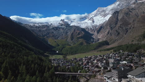 Saas-Fee-Saastal-Switzerland-aerial-drone-pedestrian-bridge-gondola-Metro-Alpin-tram-Swiss-Alpine-Alps-chalet-valley-mountain-sunmorning-glacier-Feevispa-river-yellow-orange-autumn-Larch-circle-left