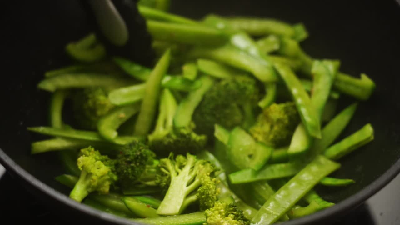 Crop cook frying fresh green beans and bell pepper with broccoli in pan