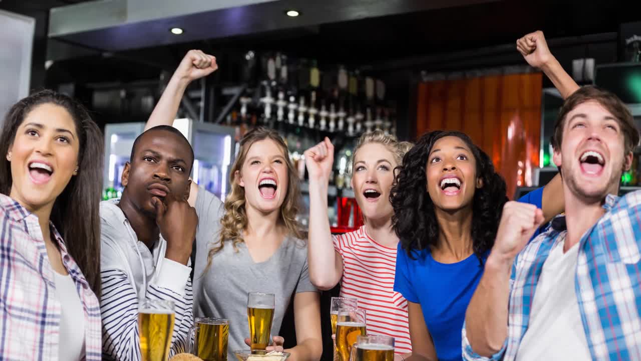 Happy diverse female and male sport fans watching game at bar, cheering and drinking