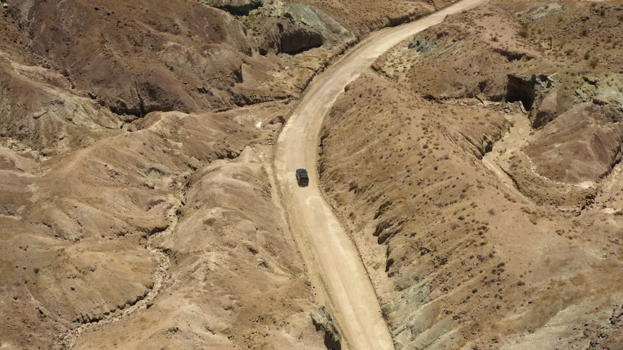 큰 검은색 suv는 모하비 사막의 무지개 분지 주변 산을 통과하는 굽은 비포장 도로를 따라 운전합니다.