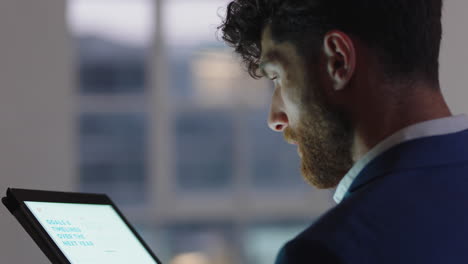 joven empresario que usa una computadora tablet trabajando hasta tarde en la oficina navegando por datos de gráficos financieros mirando las estadísticas de datos en una pantalla táctil digital
