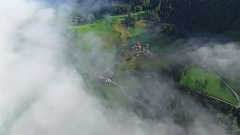 A-haven-of-simplicity-and-charm,-the-houses-and-farms-of-Val-Badia-are-beautifully-set-against-the-backdrop-of-sprawling-green-fields,-punctuated-by-the-delicate-embrace-of-morning-fog