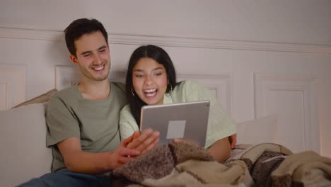 couple watching comic movie on laptop sitting on bed at home