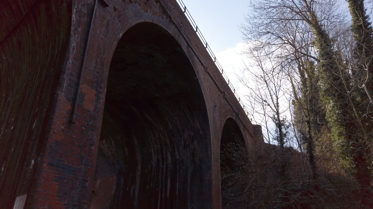 Høj buet murstensjernbanebro over en lavvandet bæk på landet