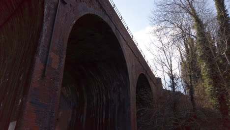 alto puente ferroviario de ladrillo arqueado sobre un arroyo poco profundo en el campo