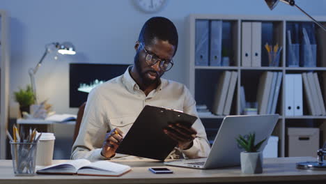 Office-Worker-Being-Still-Sitting-At-Desk-Working-With-Some-Documents-With-A-Pencil-In-The-Office-At-Night