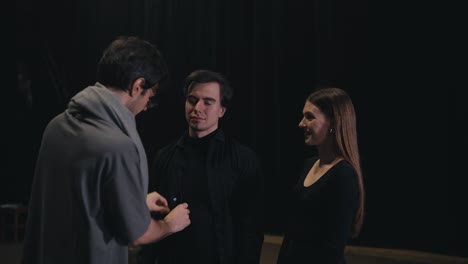 a confident brunette man in a gray t-shirt and scarf the stage director adjusts the black costumes of the actors before they go on stage during a performance in the theater