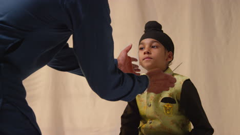 Studio-Shot-Of-Father-Tying-Turban-Onto-Head-Of-Young-Sikh-Son-Wearing-Traditional-Waistcoat-As-Sequence-Part-10-Of-10