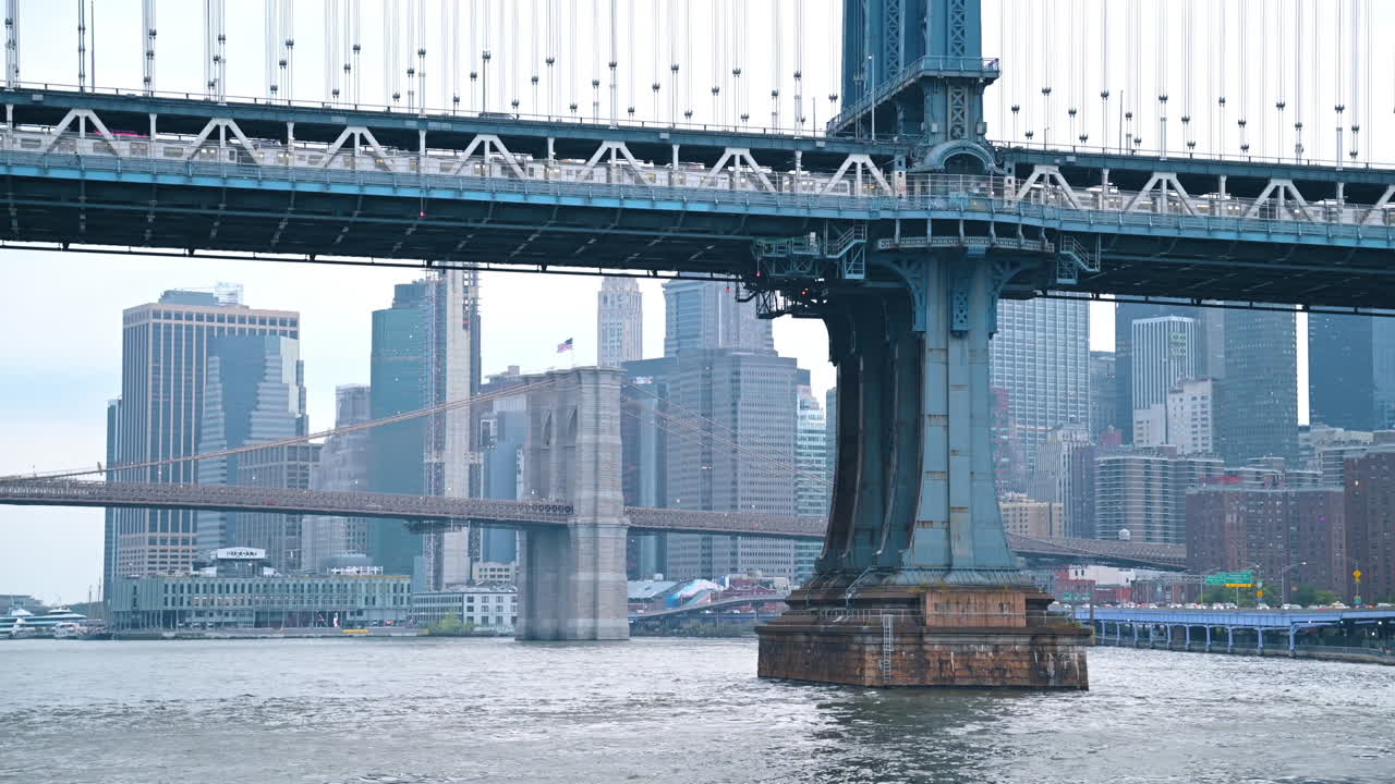 Lungo treno che attraversa il Ponte di Manhattan sull'East River. Vista dal basso di un punto di riferimento di New York dal paesaggio fluviale.
