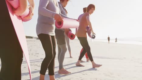 multi-ethnic group of women folding sport mats on the beach and blue sky background