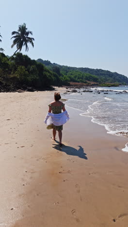 vertical drone shot behind a woman walking along a paradise beach, in sunny india