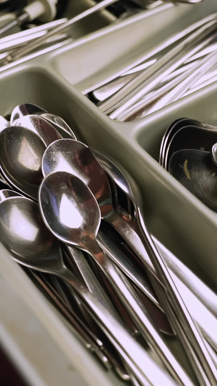 Close-up of stainless steel cutlery organized in a drawer tray—spoons, forks, and knives neatly sorted in kitchen compartments. Vertical home organization b-roll