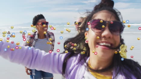 women taking selfie on sandy beach, with floating digital emoji icons for social media marketing