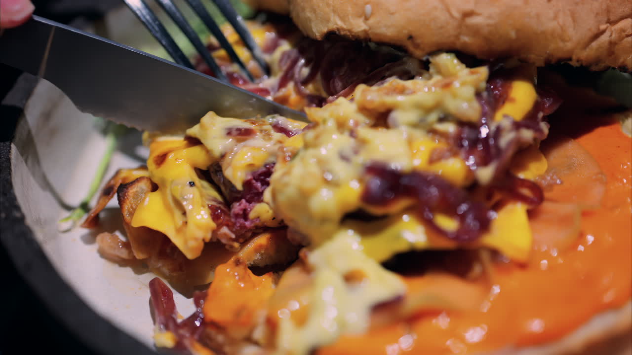 Close up of a loaded burger with melted cheese, caramelised onions, and a creamy sauce on a toasted bun being cut