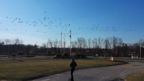 An-aerial-tracking-of-a-man-on-an-electric-skateboard-in-an-empty-park-on-a-sunny-day