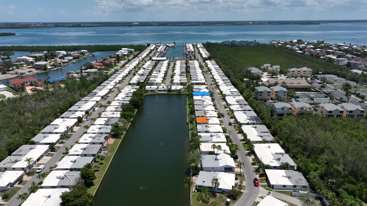 Aerial view of a coastal neighborhood with uniform white-roofed homes along a canal. Waterfront living with lush greenery and ocean views. Coquina Beach City in Florida, USA. Wide shot.