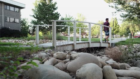 hombre camina a través de un pequeño puente peatonal en un parque al aire libre, un día soleado