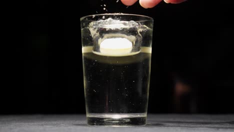 Energy-Vitamin-C-ill-tablet-falls-dropping-into-a-glass-of-water-closeup-studio-shot,-bubbles-and-frizz-inside-liquid,-medical-wellness-shot