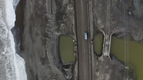 Toma-Aérea-De-Seguimiento-De-Arriba-Hacia-Abajo-De-Una-Camioneta-Que-Conduce-A-Lo-Largo-De-Una-Carretera-Inundada-Junto-Al-Océano-ártico-Cerca-De-Barrow-Alaska