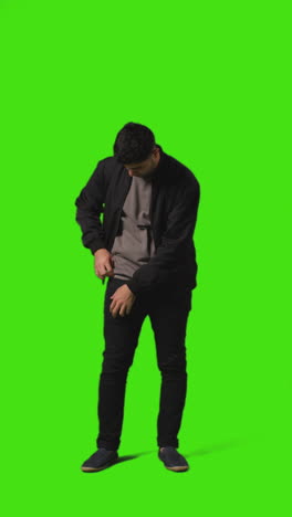 vertical video full length shot of young man answering call on mobile phone standing against green screen