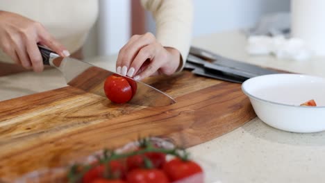 a woman slices a tomato on a wooden cutting board in a well-lit kitchen, emphasizing precision and culinary skill