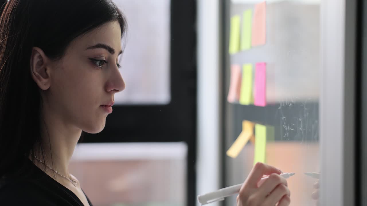 Woman writing on a glass board with sticky notes