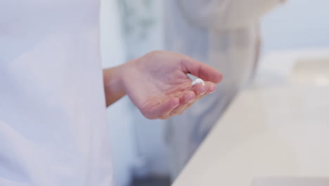 happy caucasian woman applying cream to hands in bathroom