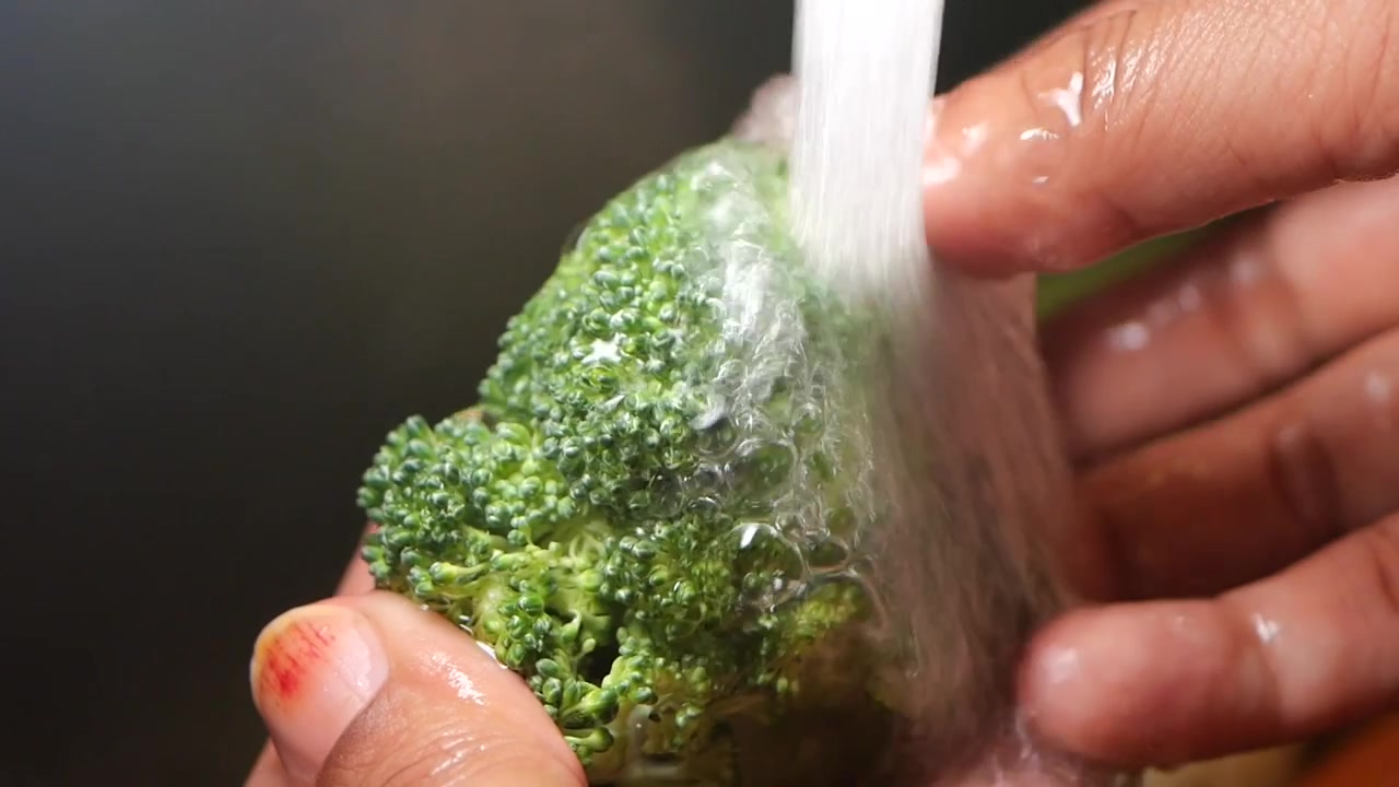 Primo piano di mani che lavano broccoli verdi freschi sotto acqua corrente