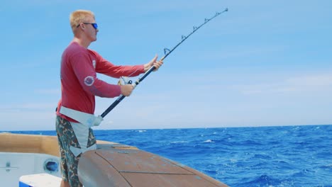 blond caucasian man reeling in a fish from a yacht