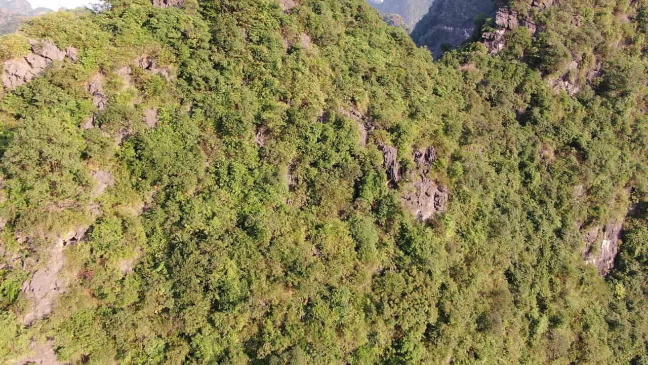 vista aérea de un avión no tripulado en vietnam volando hacia una montaña rocosa cubierta de árboles verdes en ninh binh en un día soleado