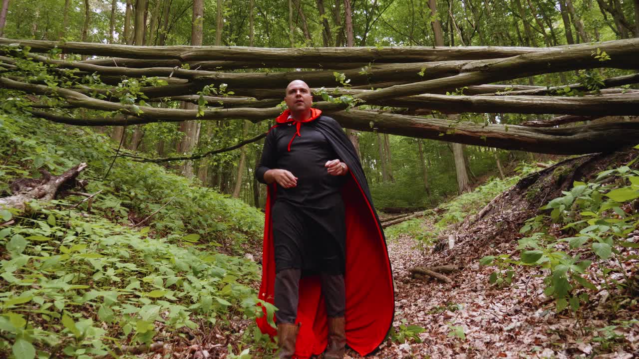 Portrait Of A Man Dressed Up In Black And Red Cape Taking Off His Hood While Walking On A Trail In The Forest