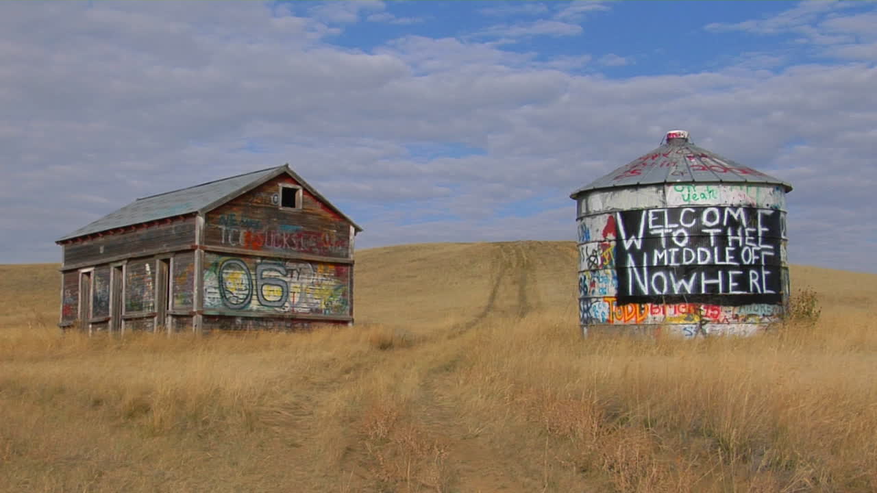una antigua casa abandonada y una torre de agua con graffiti en una pradera abierta