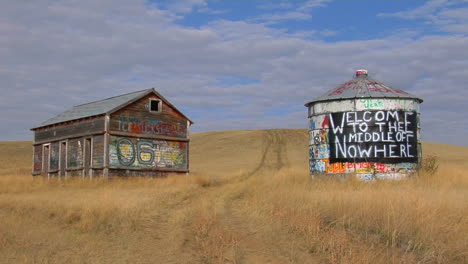 an old abandoned house and water tower with graffiti stand in an open prairie