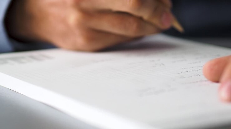 Close up shot of man hands noting something in the note book while working in the modern office