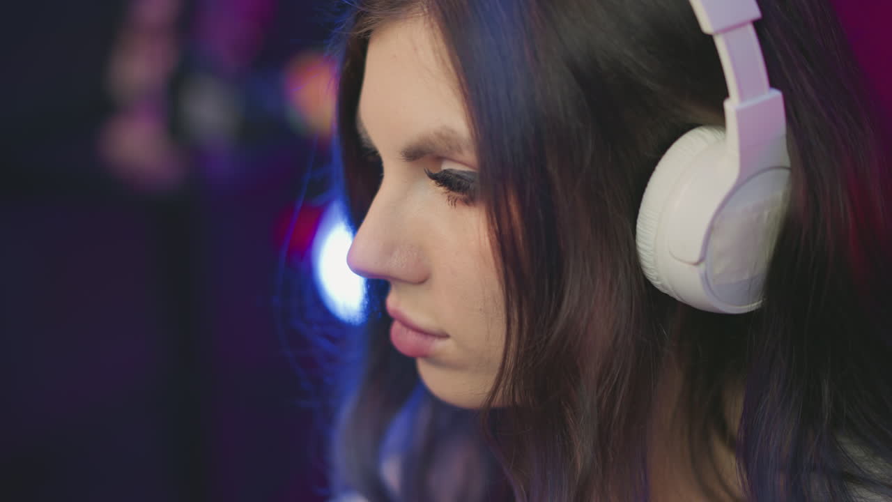 close up side view of girl with long eyelashes wearing white headphones deeply focused while colorful blurred lights glow in background creating thoughtful and immersive atmosphere