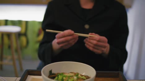 Close-Up-view-of-man's-hands-taking-chopsticks-and-starting-to-eat-noodles.-Noodles-with-vegetables.-Dinner-in-japanese