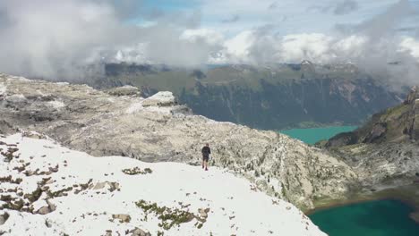 circling drone shot of a young and strong man hiking up by himself alone on top of schynige platte in the snow, wearing shorts, a jacket and backpack