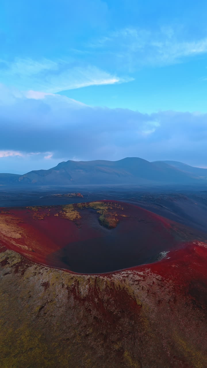 Approaching the sleeping volcano crater with red soil. Misty view of mountain range at backdrop. Iceland panorama. Vertical video.
