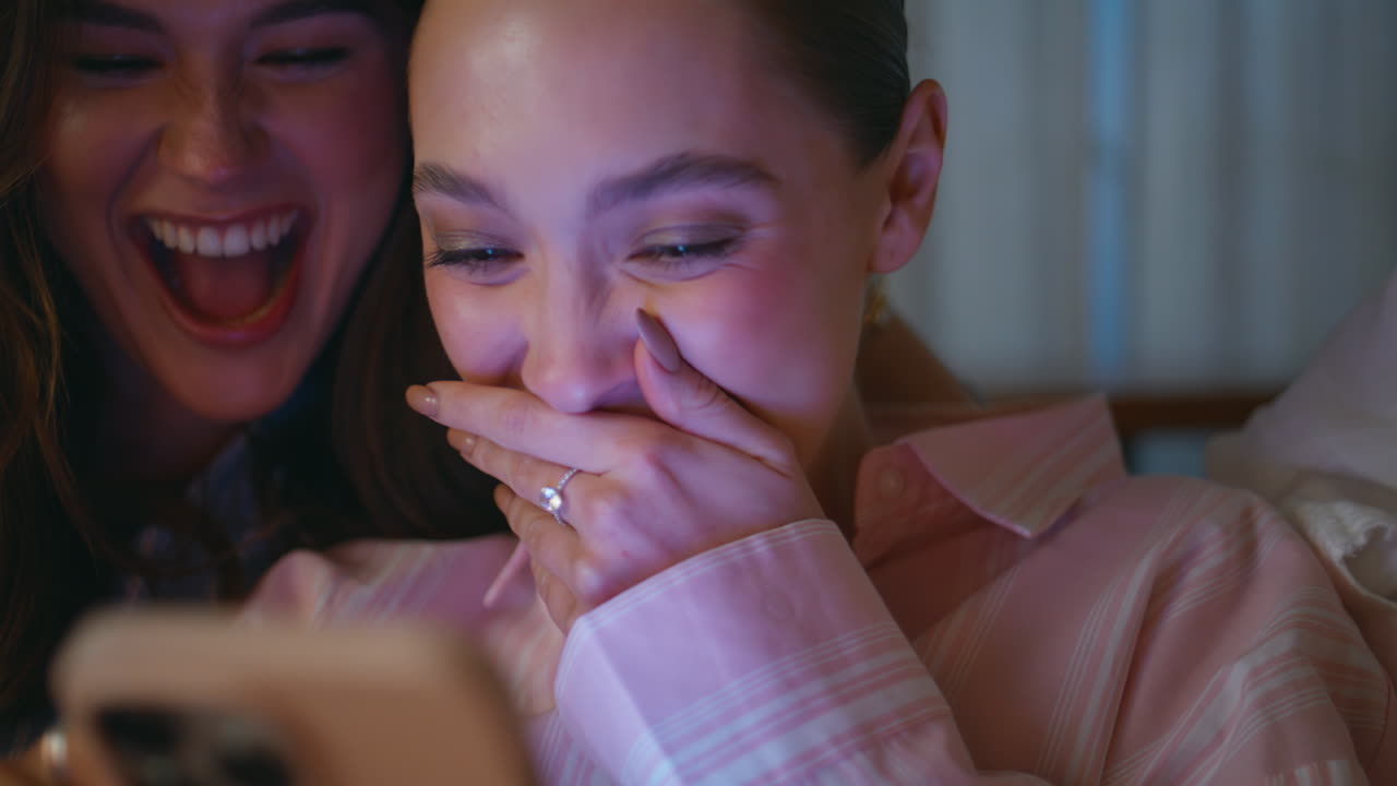 Smiling girls reading cellphone message at home pajamas party night closeup