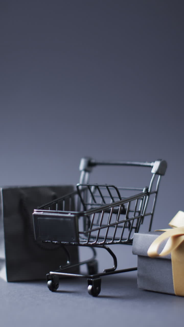 Vertical video of shopping trolley, shopping bag and gift box with copy space over grey background