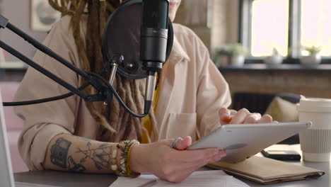 close up view of woman hands holding and tapping on a tablet while recording a podcast talking into a microphone 1